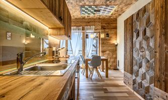 A modern kitchen with wooden surfaces and a cozy dining area. Large windows let in plenty of light, creating an inviting atmosphere.
