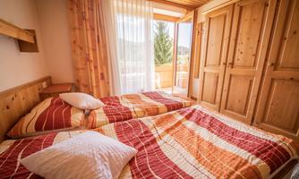 A cozy bedroom with two beds and colorful bedspreads. The room has large windows that overlook a balcony and nature.