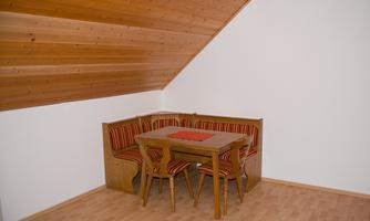 A cozy dining area with a wooden table and benches in the attic. The walls are white and the roof is clad with wooden panels.