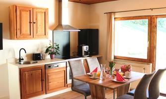 A modern kitchen with wooden cabinets and a dining area. Large windows provide plenty of daylight and a pleasant atmosphere.