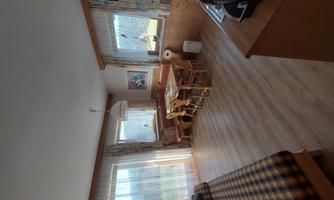 A bright room with a table and chairs, a couch, and large windows. The space is cozy and inviting with wooden decor.