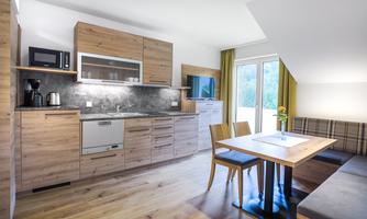 A modern kitchen room with wooden furniture and a dining table. Large windows let in plenty of daylight and offer a cozy view outside.