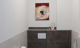 A modern toilet with simple gray tiles. An abstract painting in shades of red hangs on the wall.