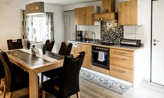 A modern kitchen with wooden cabinets and a dining area. The room is bright and invitingly designed.