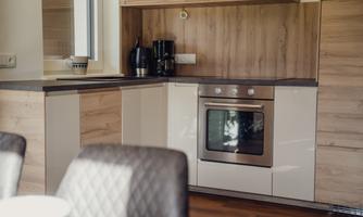 A modern kitchen with wood and white surfaces. The area includes an oven, a coffee machine, and a dining table.