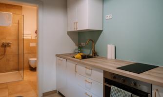 A modern kitchen with bright cabinets and a beautiful countertop. In the background, a bathroom with a shower can be seen.