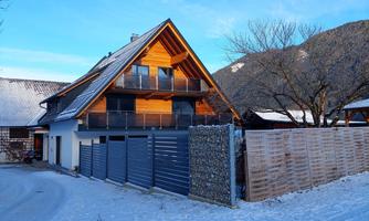 A modern house in a snowy environment. The sun is shining on the facade and the mountains are visible in the background.