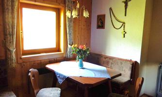 A cozy room with a table and chairs. On the table is a flower vase and there is a window with a view of light.