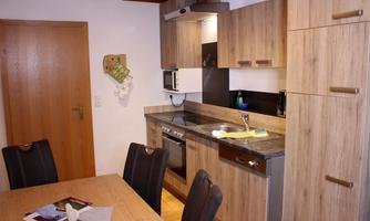 A modern kitchen with wooden cabinets and a dining table. The amenities include a stove, a sink, and connected appliances.