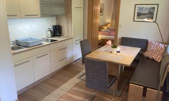 A modern kitchen with a dining table and chairs. In the background, you can see a cozy bedroom.