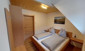 A simple bedroom with two beds and wooden shelves. A picture of a landscape is hanging on the wall.