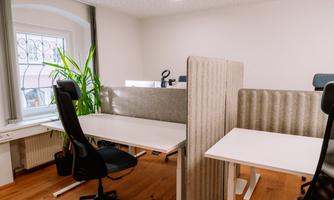 A modern office with white desks and ergonomic chairs. A plant and partition walls create a pleasant working atmosphere.