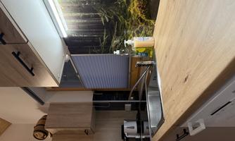 A modern kitchen with wooden surfaces and a sink. In the background, there is an image of a forested landscape.
