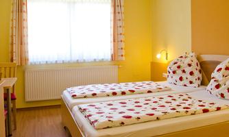 A cozy room with a double bed and colorful cushions. The room has large windows that let in plenty of daylight.