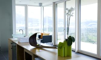 A modern furnished room with large windows and a view of nature. An orchid in a decorative vase is on the table.