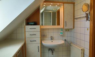 A modern bathroom with a washbasin and a large mirror. The walls are tiled and there are wooden cabinets for storage.