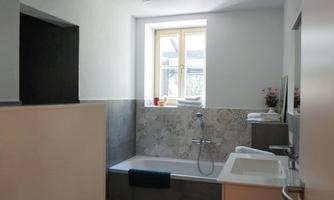 A modern bathroom with a bathtub and sink. The room is bright and friendly, with a window that lets daylight in.