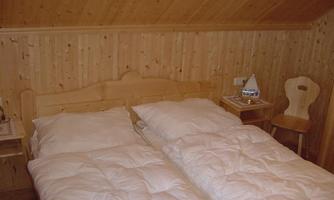 A cozy bedroom with two single beds and wood paneling. Next to the beds is a small table and a chair.