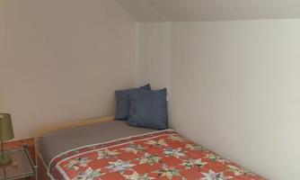 A simple bedroom with a single bed and colorful bedding. There is a nightstand with a lamp against the wall.
