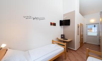 A simple room with two single beds, a television, and a window. The walls are bright and simply furnished.