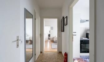 A bright corridor with doors to various rooms. On the right, a kitchen is visible, and on the left, there is a mirror on the wall.