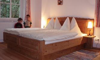 A cozy bedroom with a large double bed and wooden details. Two children are nearby exploring the room.