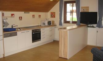 A modern kitchen with a wooden ceiling and bright floor. It is equipped with appliances such as a stove, a refrigerator, and a microwave.