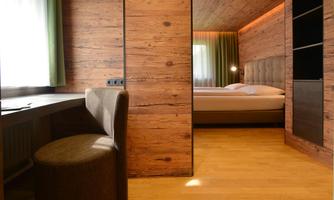 A modern hotel room with wooden walls and a cozy bed. The room is bright and well-lit, with a desk and a chair.