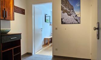 A bright hallway with gray tiles and a wooden cabinet. A picture of a mountain landscape hangs on the wall.