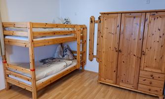 A simple room with a wooden bunk bed and a large wardrobe. The floor is made of light parquet.