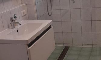 A modern bathroom with a shower and a sink. The floor is adorned with green tiles and a carpet.