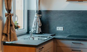 A modern kitchen with a stainless steel sink and an elegant countertop. Curtains hang in front of the window, and there is a small plant on the windowsill.
