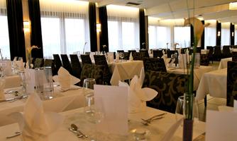 An elegant restaurant with festively laid tables and large windows. The atmosphere is inviting and modern.