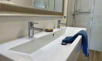 A modern bathroom with an elegant sink and a large mirror. On the countertop, there is a towel and a candle.
