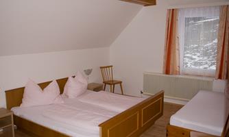A simple bedroom with two beds and an additional sofa. Bright walls and a window provide a view outside.