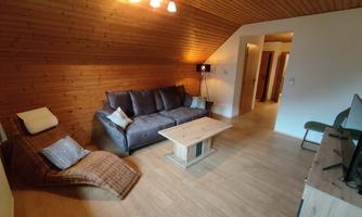 A cozy living room with wooden ceilings and a modern sofa. A coffee table and a TV corner complete the space.
