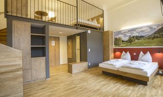 A modern room with hardwood floors and a cozy sofa bed. Above, there is a loft with additional beds.