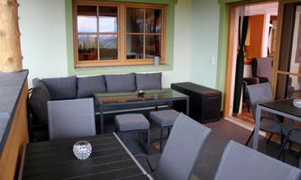 A cozy indoor area with a gray sofa, a glass table, and modern chairs. Large windows let in plenty of daylight and provide a view outside.