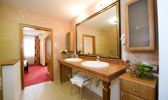 A modern bathroom with two sinks and a large mirror. In the background, a cozy room and a window with curtains are visible.