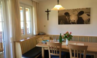 A cozy dining area with a wooden tray and chairs. A picture of a cow hangs on the wall, and the light gently falls through the windows.