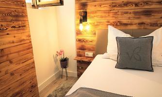 A cozy bedroom with wooden walls and a comfortable bed. Next to the bed, there is a small plant and a lamp provides warm light.