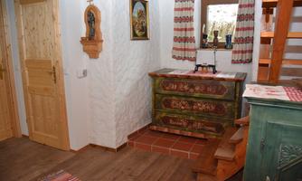 A cozy interior with wood-paneled walls and a colorful treasure chest. In the background, a staircase and some decorative elements are visible.