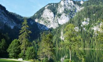 A picturesque mountain landscape with tall cliffs and dense forests. A tranquil lake reflects the surroundings.