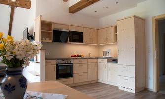 A modern kitchen with light wooden cabinets and elegant appliances. A vase with fresh flowers stands on the table.
