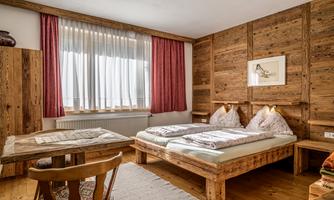 A cozy room with wooden interior and two beds. Large windows let in plenty of daylight.