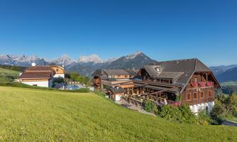 A picturesque mountain cabin surrounded by green meadows and majestic mountains. The clear sky creates a tranquil atmosphere.