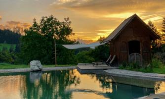 A beautiful pool in nature with a stunning sunset in the background. The rustic shed and the trees give the scene a relaxed atmosphere.