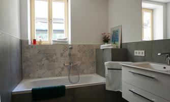 A modern bathroom with a bathtub and a sink.  
Bright windows provide plenty of daylight and a pleasant atmosphere.