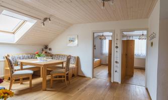 A cozy dining area with a wooden table and chairs in a bright attic room. On the left, a door to another room is visible.