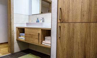 A modern bathroom with wooden shelves and a sink. Clean towels are neatly stored away, and the space feels inviting and organized.
